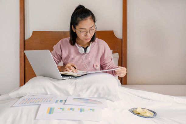 女商人拿着笔用笔记本电脑视频会议，在床上吃零食，健康食品和在家工作的概念图片下载