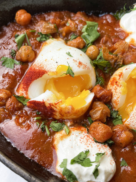 一锅地中海健康早餐的特写图片:shakshouka / shakshuka / chakchouka，鹰嘴豆，鸡蛋在番茄，辣椒，洋葱，橄榄油和大蒜的酱汁中水煮，顶部有香菜，高视图，重点在前景图片下载