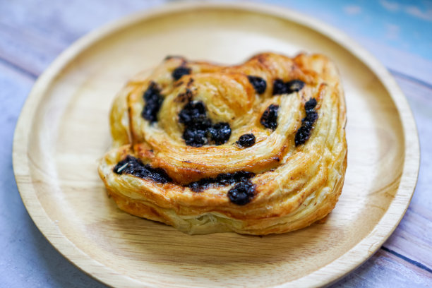侧视图照片巧克力填充丹麦葡萄干糕点在一个木制的食物盘。图片下载