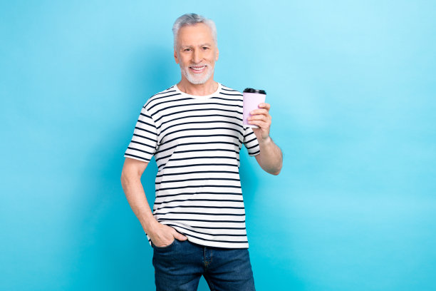 照片中，快乐的男人穿着时髦的衣服，拿着纸杯，在蓝色的背景上喝着早晨提神的咖啡因饮料图片下载