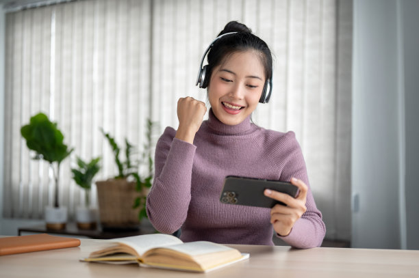 一名快乐的亚洲女性正在展示她的拳头，享受着用智能手机观看在线游戏节目的乐趣。图片下载