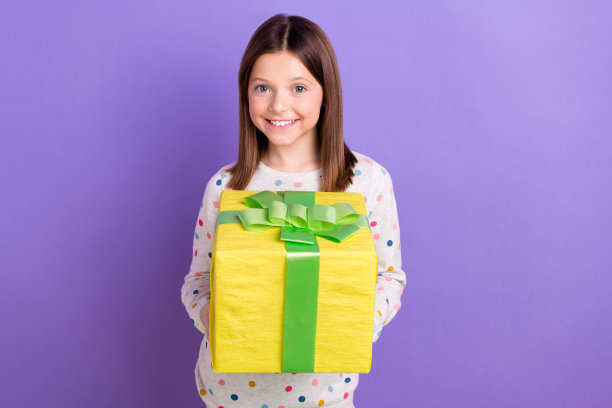 可爱的开朗的小女孩穿着带点的套头衫拿着礼物盒孤立的紫色背景的照片图片下载