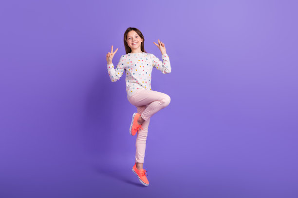 时髦可爱的小女孩的全身照片穿点毛衣跳高显示两个v字孤立的紫罗兰色背景图片下载