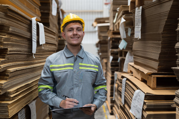 仓库男工人在瓦楞纸箱仓库工作和检查纸板质量的照片。男仓库工人检查纸板上条形码的质量图片下载