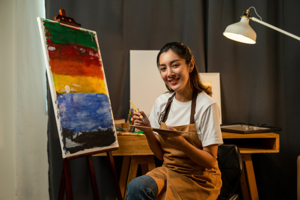 亚洲女艺术家在暗室温暖的灯光下用刷子和不同的丙烯酸颜料作画。作为艺术概念的女艺术家在创作工作室的画布上作画图片下载