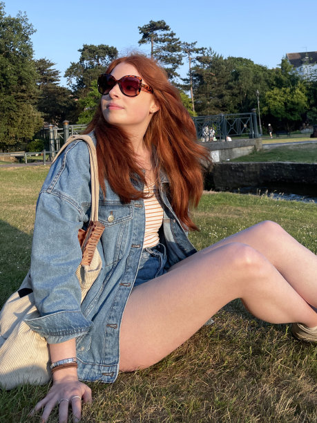迷人的红发女子坐在维多利亚时代下层花园的草坪上的特写照片，伯恩溪，伯恩茅斯，多塞特郡，英格兰，英国，湛蓝晴朗的天空，聚焦于前景图片下载