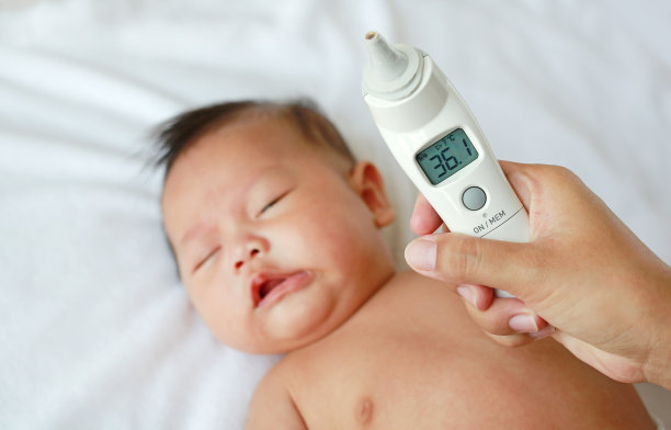 近景:母亲在家里的床上用耳朵温度计为哭闹的小男孩量体温。图片下载