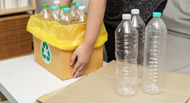 家庭回收生态绿色零概念妇女将空塑料瓶扔进装有黄色垃圾袋的回收箱。图片下载