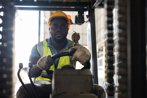 非裔美籍男性工人，在工业仓储工厂仓库驾驶和操作叉车搬运产品或包裹货物图片下载