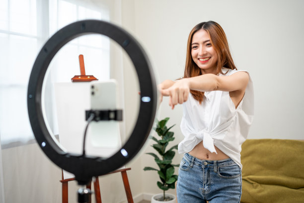 年轻的时尚影响者亚洲女人在家里的客厅里用手机跳舞。创作者，视频博主，才艺舞蹈，享受爱好，内容录制，展示视频分享在社交媒体上。图片下载