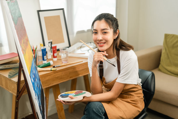 亚洲女艺术家正在用画笔和不同的丙烯酸颜料作画。作为艺术概念的女艺术家在创作工作室的画布上作画图片下载