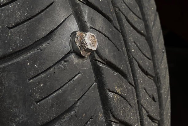 关闭按钮头针金属螺丝钉卡住刺入车轮轮胎上的道路。卡在螺栓上的汽车无内胎轮胎。破碎的汽车轮胎带被尖锐的金属钉钉住的照片。图片下载