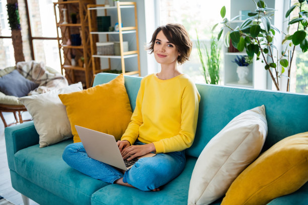积极开朗的女士坐在沙发上，在公寓里用现代科技上网本远程学习的照片图片下载