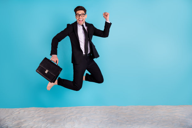 全身照片正面酷男人穿黑色西装箱跳高赢得暑假孤立的蓝色背景图片下载