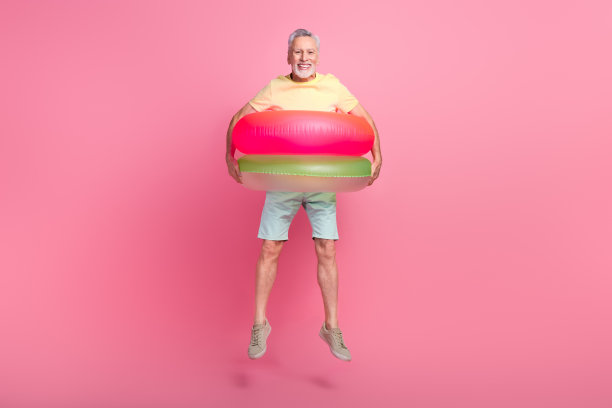 全身尺寸的照片横幅跳跃无忧无虑的旅游老人戴着两个充气环孤立在粉红色的背景图片下载