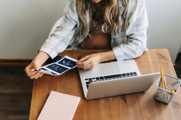 一位孕妇坐在她的工作场所看着她的孩子的超声波。图片下载