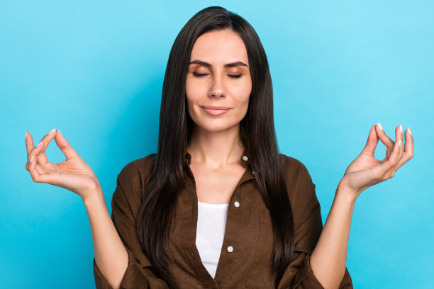 漂亮的梦幻女孩穿着棕色衬衫，闭着眼睛享受瑜伽孤立的蓝色背景的照片图片下载
