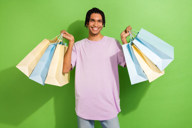 照片中的酷时髦的人笑容满面，双手拿着商场购物袋孤立的绿色背景图片下载