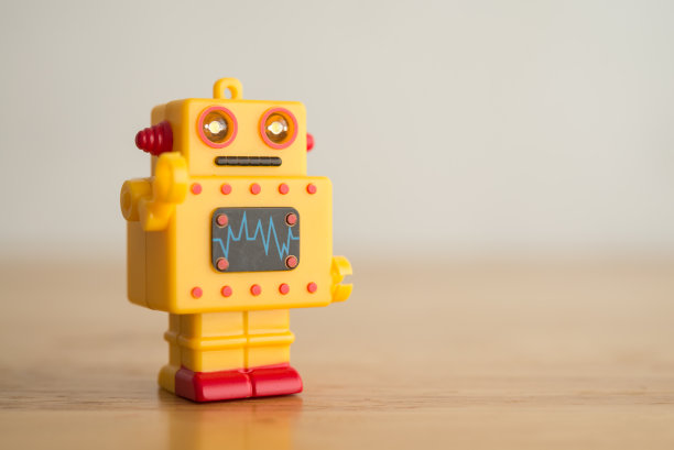 黄色可爱的复古AI机器人玩具在木制背景复制空间。图片下载
