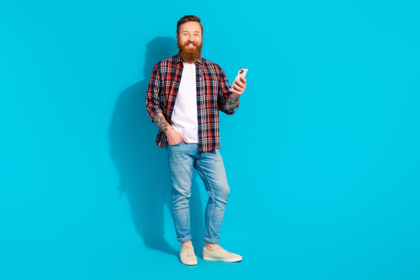 自信的潮人胡子男人纹身商人的全身照片浏览手机好消息互联网孤立的蓝色背景图片下载