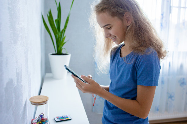 一个可爱的少女用智能手机与她的朋友和同学通过互联网进行视频交流。写留言或通过免提电话讲话图片下载