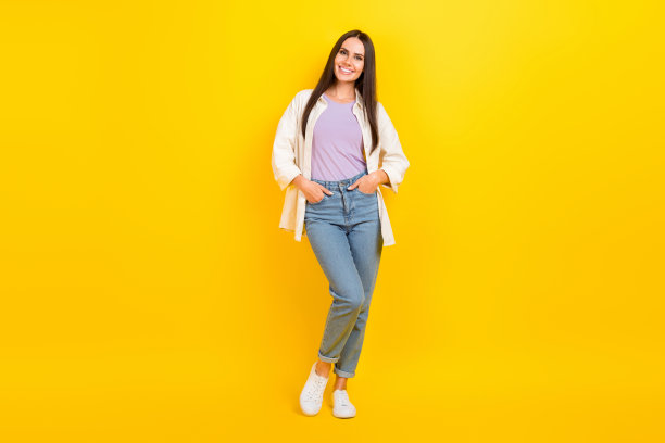 全尺寸照片的华丽漂亮的女孩穿着白色衬衫牛仔裤子，手臂在口袋里站孤立的黄色背景图片下载