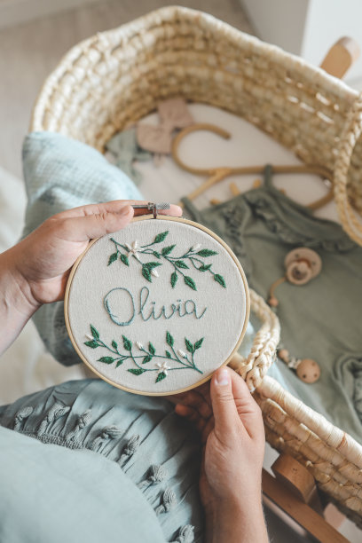 一位孕妇手里拿着手工刺绣，上面写着Olivia的名字，充满期待图片下载