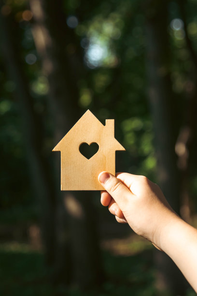 手拿着一个阳光普照的木屋模型，背景是森林。图片下载