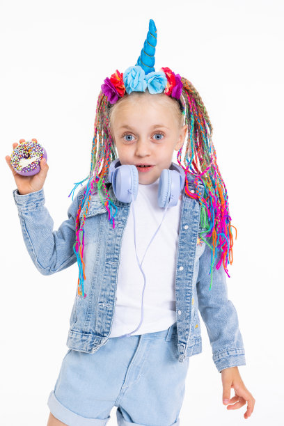 小女儿的特写照片，她梳着彩色的辫子，戴着蓝色玉米和花朵的独角兽发带，穿着时尚的牛仔服装，戴着紫色的耳机，手里拿着甜甜圈图片下载