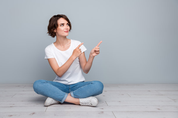 漂亮女孩的全身照片穿着时尚的t恤，坐着看，表明在折扣空空间孤立的灰色背景图片下载