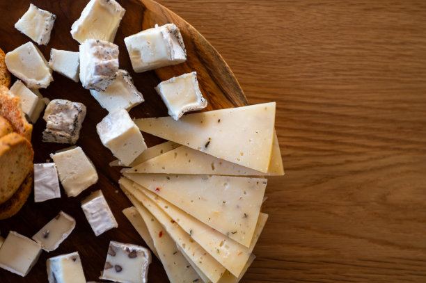 不同种类的奶酪，有发霉的，有硬的，有香料的等等，放在木桌上的一个木盘上。美味健康的葡萄酒小食。从上面看。有选择性的重点图片下载
