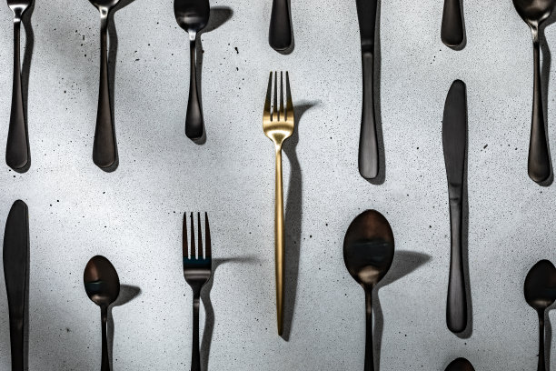 一把金色的叉子夹在黑色的餐具中间。中性灰色混凝土背景图片下载