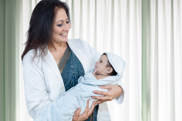 年轻的印度女医生或护士抱着裹在毯子里的新生儿。医院病房里医护人员抱着婴儿的照片。图片下载