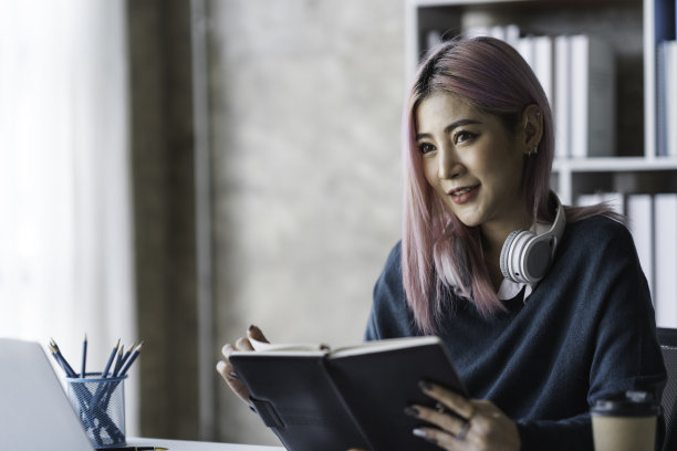 亚洲女商人坐着吃面包，看手机，读课间书，在办公室放松，愉快而美味地工作。图片下载