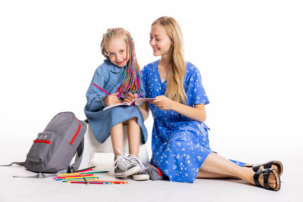 快乐的小学女生与年轻金发母亲在白色地板上摆姿势，拍摄返校概念照片图片下载