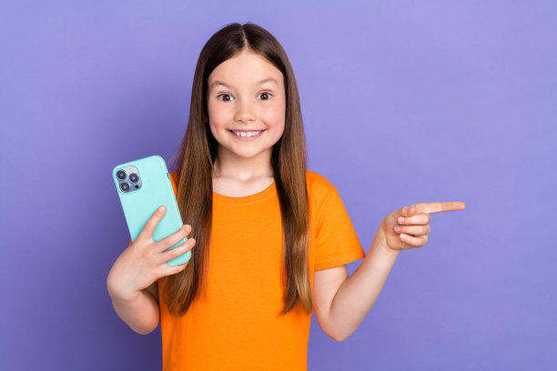 照片兴奋有趣的小女生孩子橙色t恤点手指模型与手机难以置信孤立的紫色背景图片下载