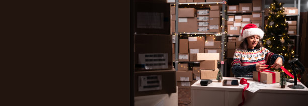 快乐的女圣诞老人在车间用红丝带包装礼物盒，准备送货包裹。圣诞快乐送货理念。图片下载