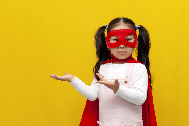 亚洲小女孩穿着超人的服装，戴着面具，双手伸向一边，为复制空间做广告图片下载