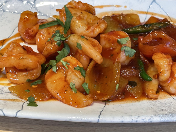 餐厅设置的特写图片，盘子里有糖醋对虾，用红洋葱、红辣椒、蒜瓣、鲜姜、糖、麦芽醋、酱油和番茄酱调味，重点放在前景图片下载
