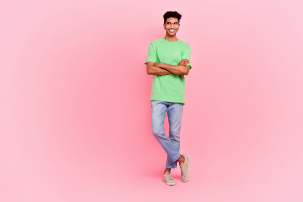 英俊男子的全身照片，戴着耳环，穿着时尚的t恤，双臂折叠，在粉红色的背景下看起来空无一物图片下载
