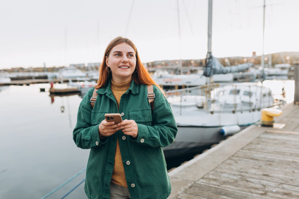 快乐的旅游女孩用智能手机在欧洲旅行。度假的概念，探索有趣的地方旅行租船。女人沿着海滨散步。高质量照片图片下载