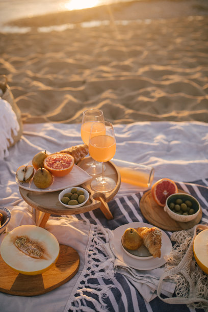 美丽美味的野餐，柠檬水，新鲜水果和牛角面包在日落的海滩。图片下载