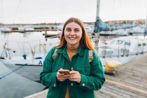 快乐的旅游女孩用智能手机在欧洲旅行。度假的概念，探索有趣的地方旅行租船。女人沿着海滨散步。高质量照片图片下载
