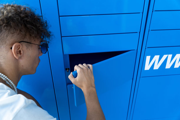 一名男子打开一个蓝色储物柜取包裹。网上购物，电子商务和包装的概念图片下载