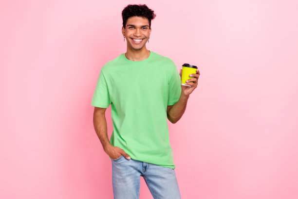 照片中，一个穿着绿色时髦衣服的快乐时髦的家伙在粉红色的背景下散步，享受着咖啡因的清爽饮料图片下载