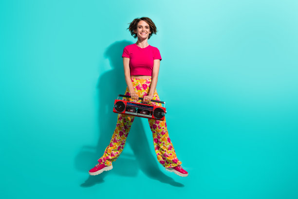 漂亮闪亮的女士花印花裤的全身照片跳高听立体声歌曲孤立的绿松石色背景图片下载