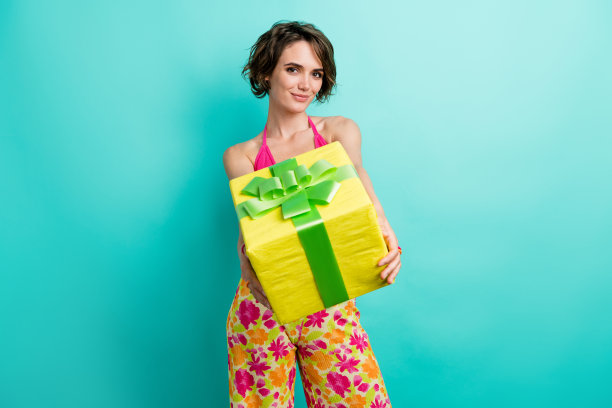 照片漂亮可爱可爱的女孩穿着时髦的衣服，手拿盒子给你的礼物孤立的青色背景图片下载