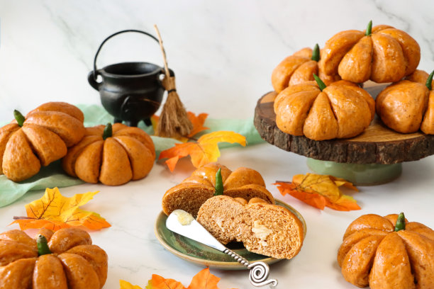 图片上是半切的自制的涂了黄油的万圣节小面包，盘子上涂着杏果酱，蛋糕架上堆着南瓜设计的卷，上面有绿辣椒梗，黑色的大锅，秋天的叶子，大理石效果的背景，重点放在前景上图片下载