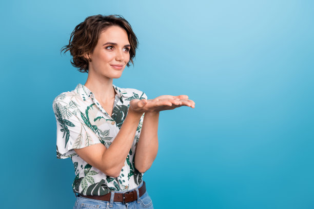 漂亮的年轻女孩的照片肖像手掌拿着促销空空间穿时髦的印花树叶装孤立的蓝色背景图片下载