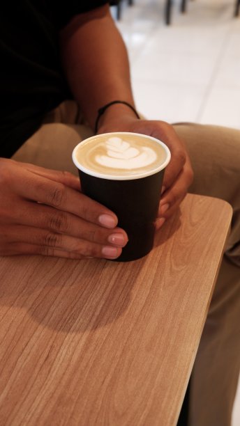 男人手里拿着热咖啡。在咖啡馆或咖啡店的木桌上手持咖啡杯图片下载
